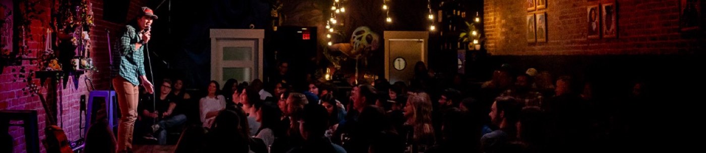 A comic on the Main Showroom stage at Mic Drop, playing to a full room of exposed brick and warm stage light